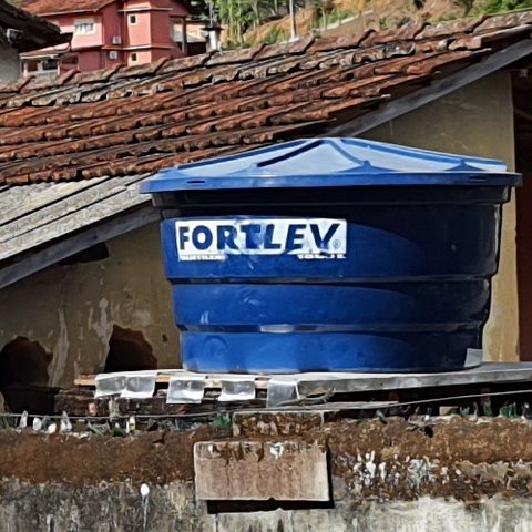 Caixa d'água azul de polietileno sobre o telhado de uma casa